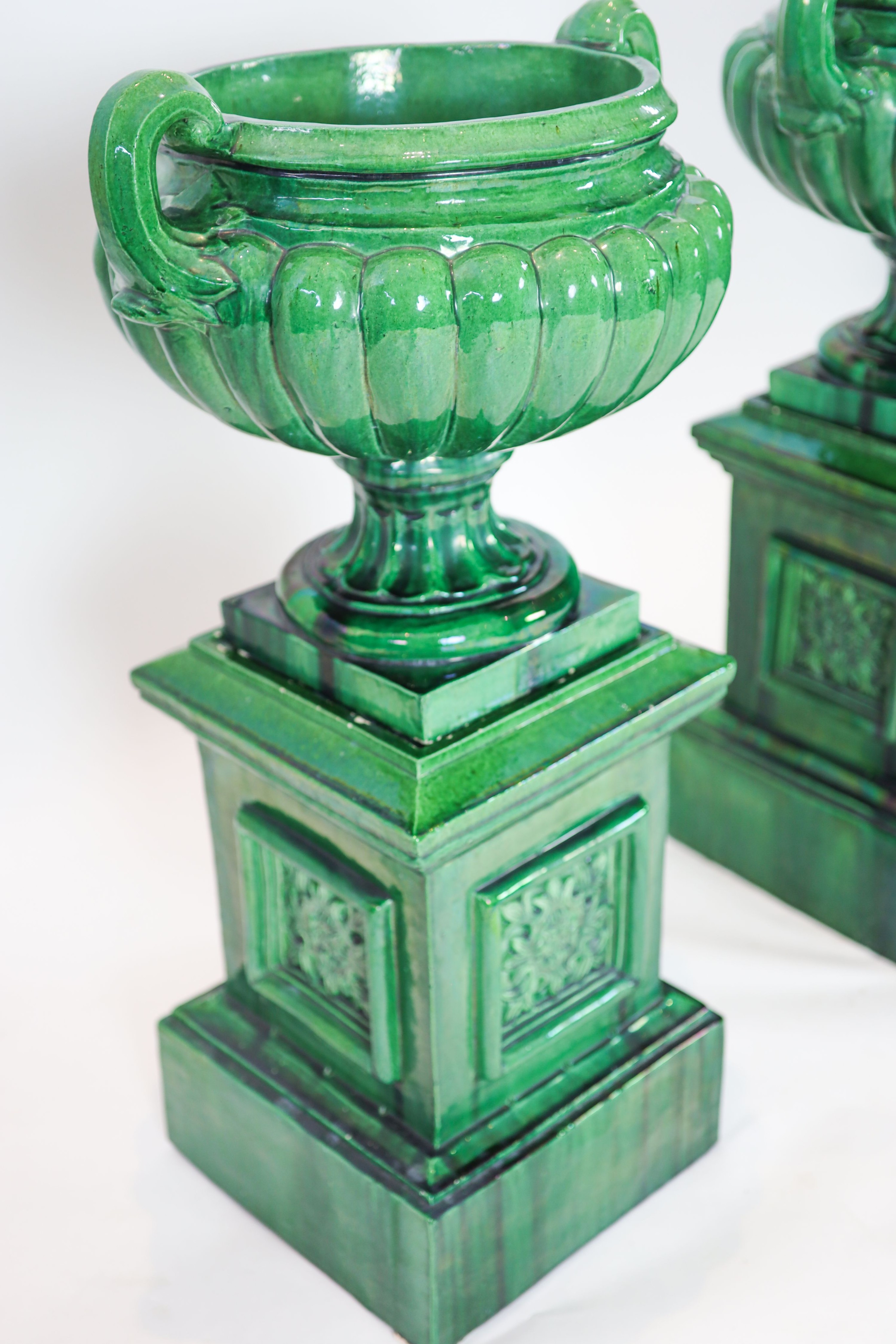 A pair of large dark green glazed terracotta fluted urns, raised on square plinths, diameter 50cm, height 101cm